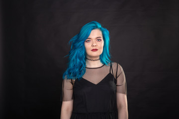 Style, fashion and hair concept - close-up portrait of young woman in black dress with blue hair on black background
