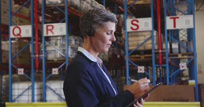 Female warehouse manager talking with headset in loading bay 4k