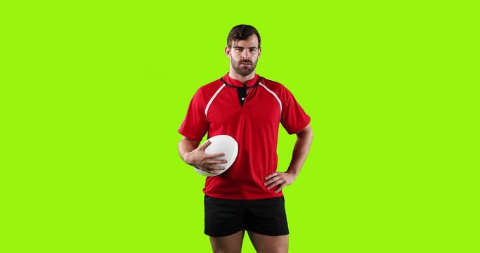 Professional rugby player standing and holding a ball on green background 4k