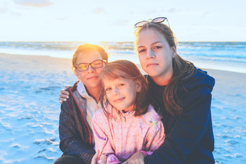 Fototapeta na wymiar Three sisters on the sea beach at sunset hugging each other