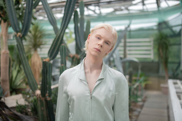 Model standing near cactuses while posing in greenhouse
