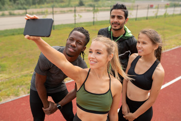 Pretty blonde girl in activewear making selfie with her friends on stadium