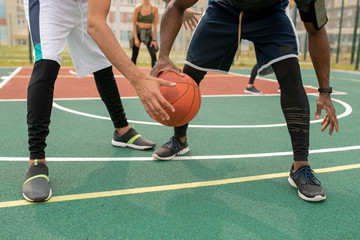Young intercultural sportsmen in activewear playing basketball on outdoor court