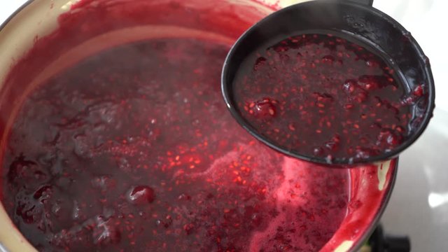 Woman puts handmade berry jam in jar. Boil raspberry jam. Vibrant colors in sunlight.