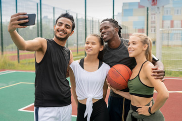 Fototapeta na wymiar Group of young intercultural friends in sportswear making selfie on court