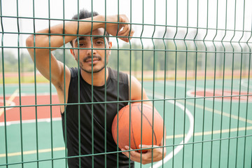 Serious male basketball player with ball standing against net