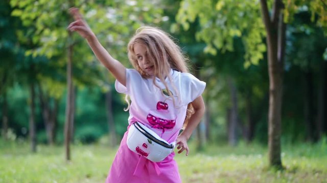 Slow motion of a girl with long hair dancing outdoors. Beautiful little girl in t-shirt and shorts posing to camera on the natural background in summer.