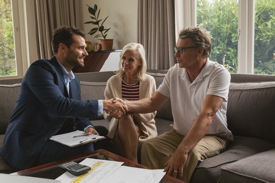 Active senior man shaking hands with real estate agent in living room