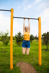 Fototapeta premium Beautiful young woman hanging on the horizontal bar. Sports and physical education.