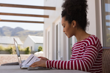 Woman looking at documents while using laptop at home