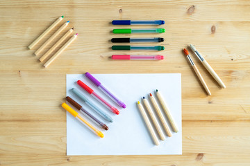 Obraz premium View of blank paper and several sets of crayons and pens and two paintbrushes