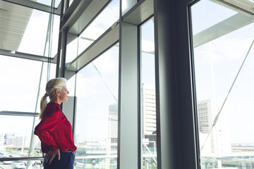 Senior businesswoman with hands on hip looking through window in office building