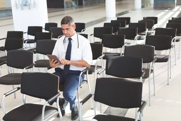 Male doctor sitting on chair and using digital tablet in conference room