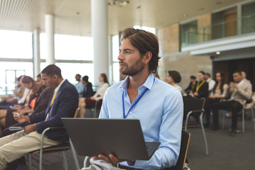 Young businessman with laptop looking away during seminar