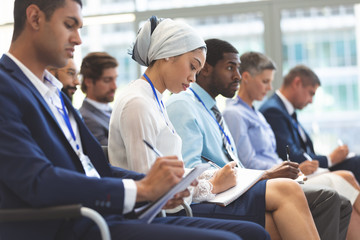 Business people writing on notepad during seminar