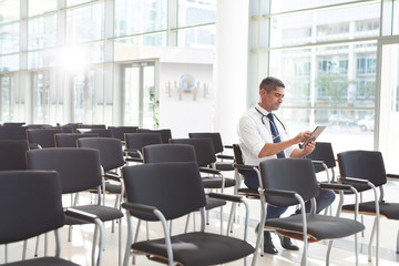 Male doctor sitting on chair and using digital tablet in a conference room