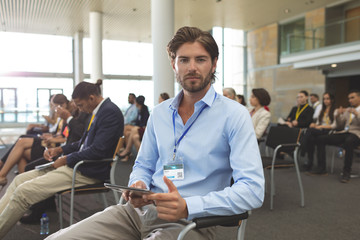 Young businessman with digital tablet looking at camera during seminar