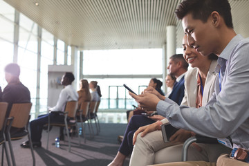 Business executives discussing over mobile phone during seminar