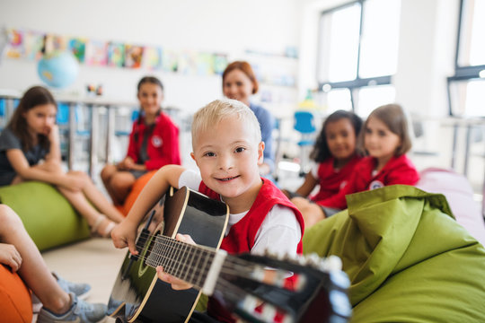 A down-syndrome boy with school kids and teacher sitting in class, playing guitar.
