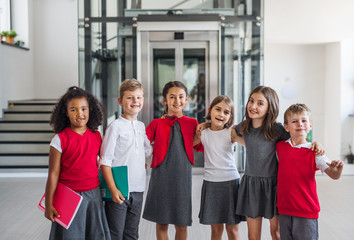 A group of cheerful small school kids in corridor, looking at camera.