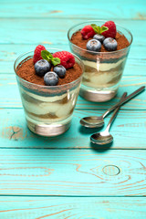Classic tiramisu dessert with blueberries and strawberries in a glass cup on wooden background