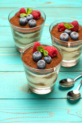 Classic tiramisu dessert with blueberries and strawberries in a glass cup on wooden background