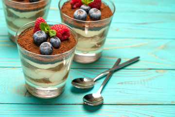 Classic tiramisu dessert with blueberries and strawberries in a glass cup on wooden background