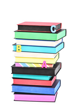 Stack of colorful books witch different sprayed edges and scattered letters spelling ABC, isolated on white background.