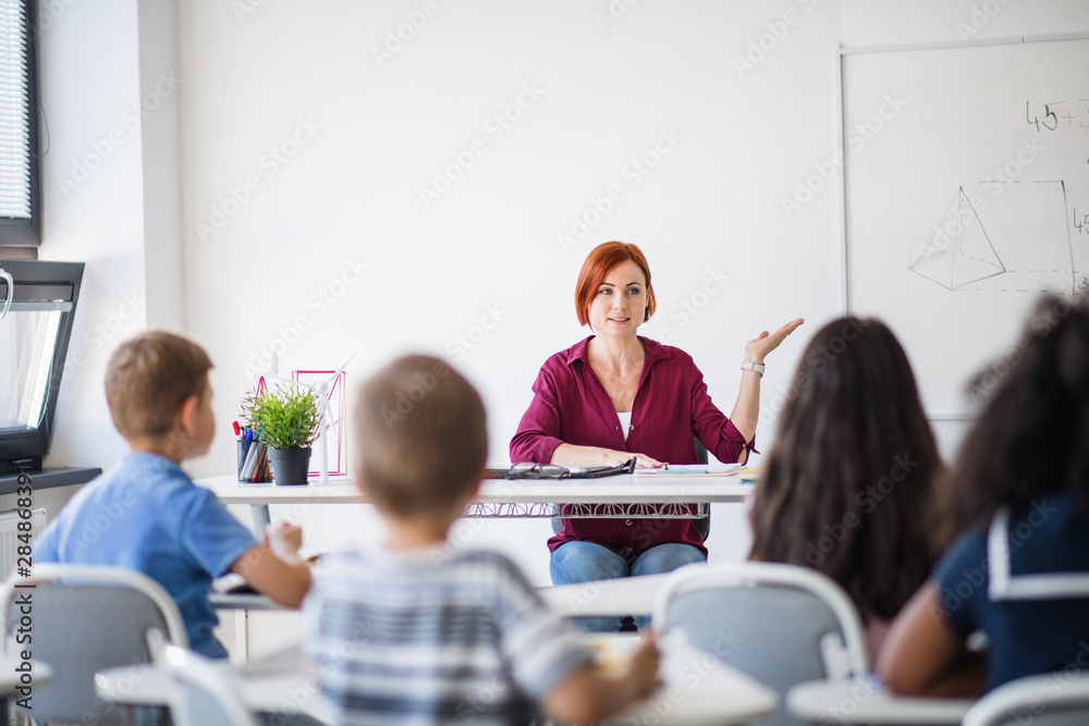 Sticker rear view of school children sitting at the desk in classroom, listening to teacher.