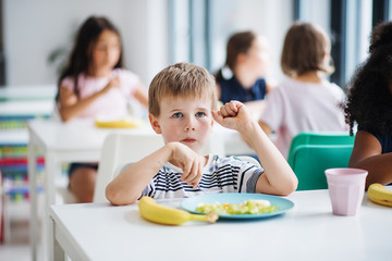 A group of cheerful small school kids in canteen, eating lunch.