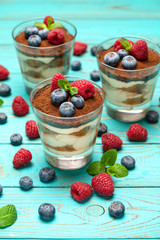 Classic tiramisu dessert with blueberries and strawberries in a glass cup on wooden background