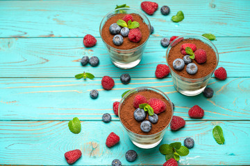 Classic tiramisu dessert with blueberries and strawberries in a glass cup on wooden background