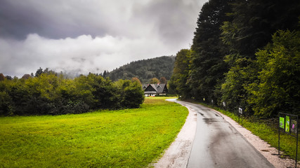 Fototapeta na wymiar Countryside road, foggy, cloudy and rainy day in national park Triglav in Slovenia. Village Stara Fuzina by the Bohinj lake.