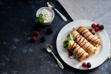 Pancakes with curd filling. Watered with chocolate topping on top, decorated with raspberries and blackberries. In bowls of berries and curd cream.  