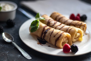 Pancakes with curd filling. Watered with chocolate topping on top, decorated with raspberries and blackberries. In bowls of berries and curd cream.  