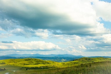 Hills with green grass and blue sky with white puffy clouds