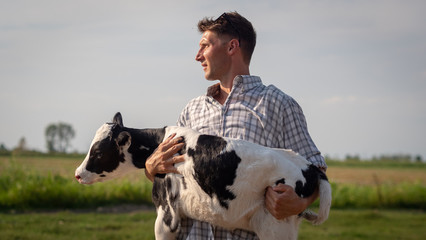 Authentic shot of young man farmer is holding on his arms an ecologically grown newborn calf used for biological milk products industry on a green lawn of a countryside farm.  © Kitreel