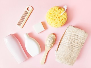Flat lay bath products. Pink shampoo bottle, shower gel, soap bar, wooden hair brushes, yellow sponge and terry towel