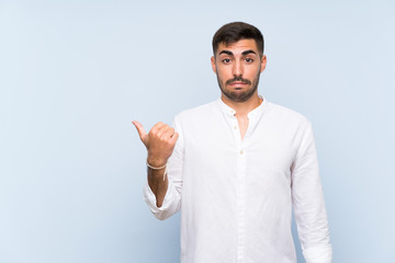Fototapeta premium Handsome man with beard over isolated blue background unhappy and pointing to the side
