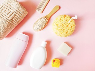 Bath products, cosmetics for skin and hair care flat lay photo. Beige towel, shower gel, shampoo, wooden comb, soap bar, yellow sponge, rubber duck on a pink background