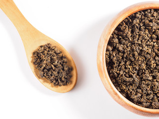 Fermented granular tea from Cherry (Cerasus) leaves in wooden cup with spoon on white background