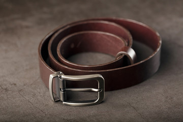 Fashionable men's brown belt made of genuine leather with a light metal buckle on a dark background. Genuine leather, handmade