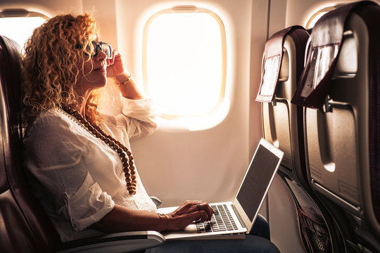 Business adult curly blonde woman travel on airplane connected to internet with modern computer laptop - people on work everywhere and digital nomad free lifestyle concept -flight on boad services