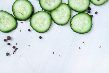 Slices of fresh cucumber and spices. Close-up on a white wooden background.