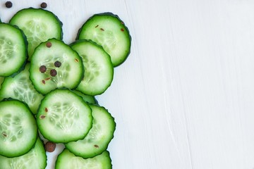Slices of fresh cucumber and spices. Close-up on a white wooden background.