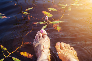 Female feet dipped in the water of a forest lake with beautiful water flowers