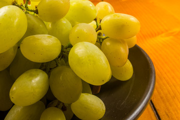 large brush of green grapes in a dark ceramic plate on a wooden background