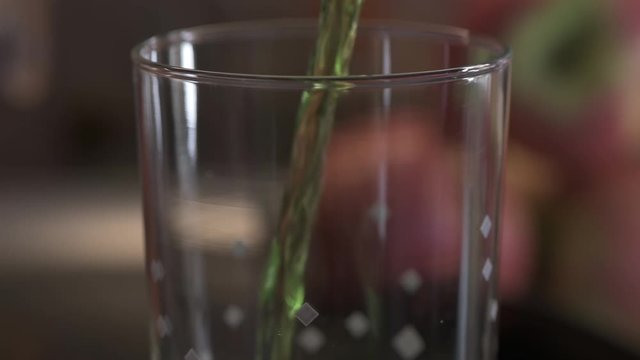 Green estragon drink pouring into water glass with lot of sparkling bubbles. Full HD 60 fps footage with shallow depth and blurring bokeh.