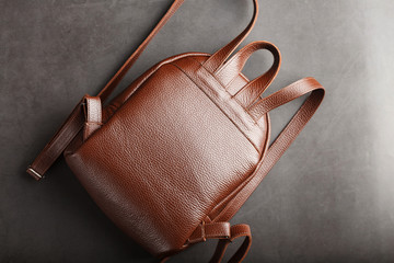 Brown backpack made of textured brown leather on a black stone background. Elegant golden brown women backpack with fashion and rivets