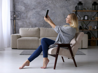 A girl sits in a chair and takes pictures on a tablet. Comfortably work at home remotely via video. Copy space.